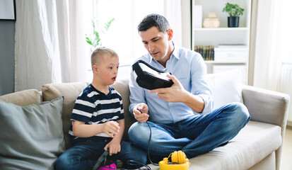 Father with happy down syndrome son indoors at home, using vr goggles.