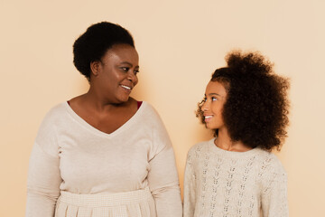 african american grandmother and granddaughter looking at each other on beige background