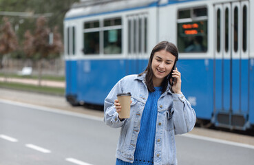 Fototapeta premium Stylish girl in casual style on a walk in the city speaks by phone.