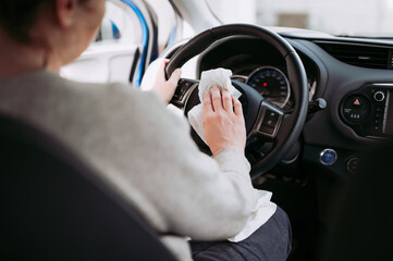 Female driver taking care of car interior hygiene. Woman's hand cleaning steering wheel of modern vehicle, using wet wipes.