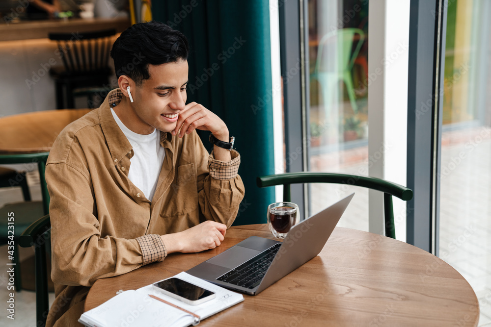 Wall mural young hispanic man student sitting at the cafe table indoors