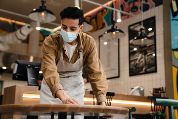 Young waiter disinfecting table in cafe