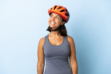 Young cyclist woman isolated on blue background thinking an idea while looking up