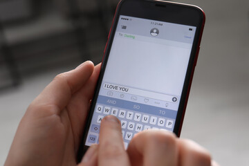 Woman sending message with text I Love You indoors, closeup