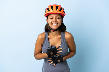 Young cyclist woman isolated on blue background smiling a lot - obrazy, fototapety, plakaty