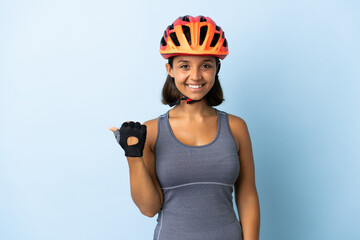Young cyclist woman isolated on blue background pointing to the side to present a product - obrazy, fototapety, plakaty