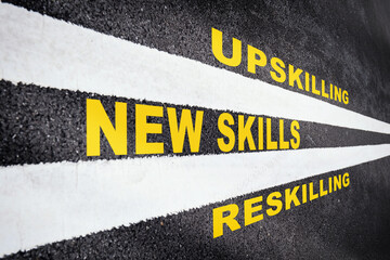 New skills development concept and changing skill demand idea. New skills, reskilling and upskilling written on asphalt road with white marking line - obrazy, fototapety, plakaty
