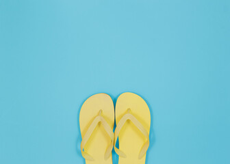 Top view of a pair of simple yellow flip flops. Light blue background.