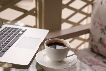 Cup of aromatic morning coffee and laptop on table in cafe