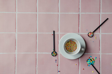 Colourful candy sprinkles in a white coffee cup and 3 black teaspoons for dessert filled with...