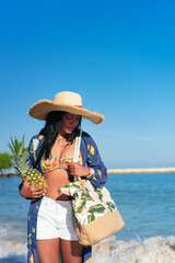 African Woman holding a pineapple while walking on the beach