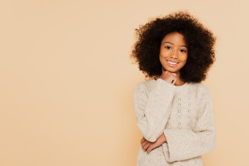 smiling preteen african american girl with hand near face isolated on beige