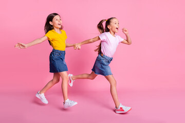 Full length body size view of two pretty cheerful girls holding hands jumping running isolated over...