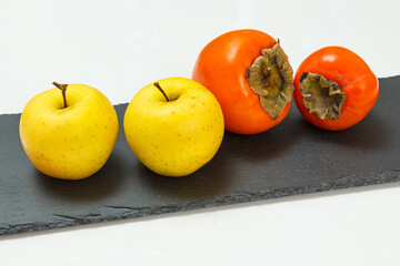 Apple fruits and ripe persimmon fruits on the black stone board.