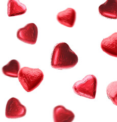 Delicious heart shaped chocolate candies wrapped in red foil falling on white background
