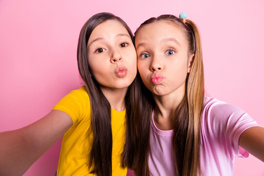 Self-portrait of attractive funny girlish pre-teen girls hugging sending air kiss isolated over pink pastel color background