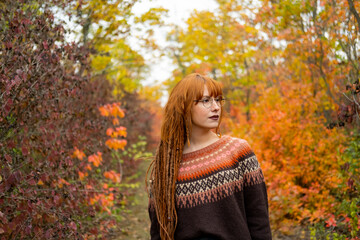 Young woman with red dreadlocks and wearing a sweater in the beautiful autumn forest - 435429305