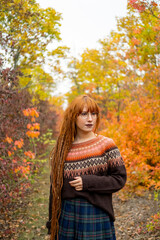 Young woman with red dreadlocks and wearing a sweater in the beautiful autumn forest