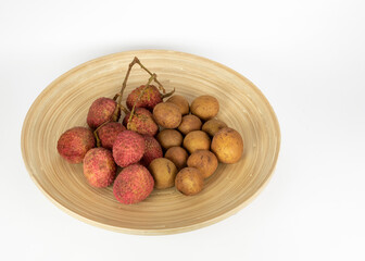 Lychee and longan fruit are displayed on a round wooden plate against a white background.