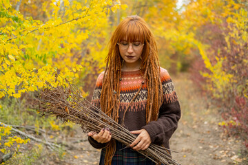 Young woman with red dreadlocks and wearing a sweater in the beautiful autumn forest