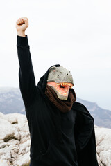 Caucasian male activist wearing a dinosaur mask and cape raising his fist in the Sierra de...