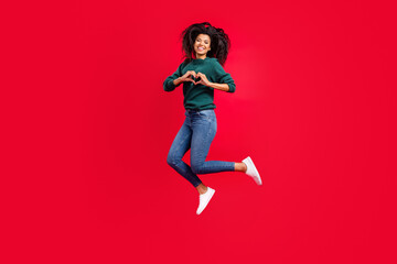 Photo of sweet charming dark skin woman dressed green pullover smiling showing fingers heart jumping isolated red color background