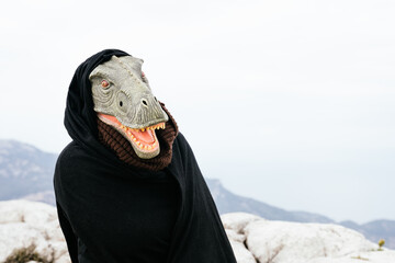 Caucasian man with a dinosaur mask and a cape making a questioning gesture with his body in the...