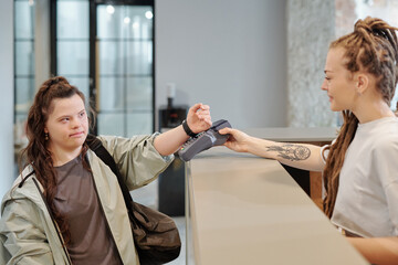 Contactless payment being made by disable girl with Down syndrome over reception counter in fitness...