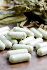 Pile of herbal medicine in capsules with herb dry leaf.