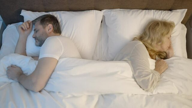 Middle-aged couple sleeping separately in bed, relationship problems, crisis