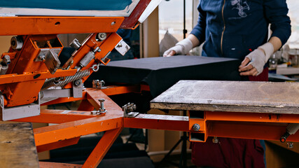 selective focus photo of print screening apparatus and worker. serigraphy production. printing images on t-shirts by silkscreen method in a design studio