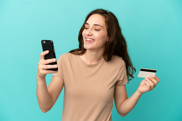 Fototapeta premium Young caucasian woman isolated on blue background buying with the mobile with a credit card