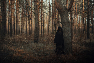 dark portrait of a terrible witch in a black suit in the forest