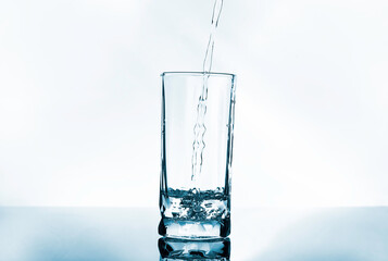 Pouring purified fresh drinking water and bubbles into transparent glass and droplets on selection floor.