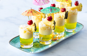 platter of pineapple jelly parfaits garnished with pineapple wedges, cherries and mini umbrellas ready for a party.