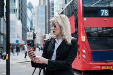Belle femme d& 39 affaires utilisant un smartphone dans la ville de Londres. Bus rouge derrière.