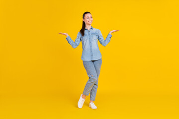 Fototapeta na wymiar Full length photo of charming pretty lady dressed jeans shirt showing scales arms empty space isolated yellow color background