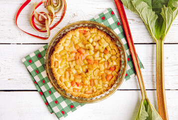 Above view of homemade round baked rhubarb ( Rheum hybridum ) pie white rustic wood table background. Rhubarb stalks on side. Seasonal spring dessert.