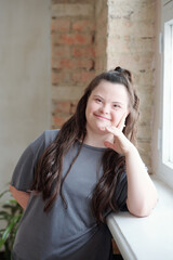 Happy disable girl in grey sportswear looking at you while leaning by windowsill