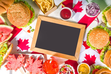 Naklejka na ściany i meble Set of various Canada Day bbq food. Picnic party table with maple leaf shaped watermelon, flags, burgers, hot dogs, fries and sauces, cold drinks, white table with red decor, top view copy space