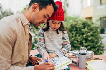 Closeup of loving father drawing with his daughter in red hat outdoors after school. Father...