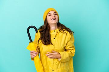 Young caucasian man holding an umbrella isolated on blue background smiling a lot