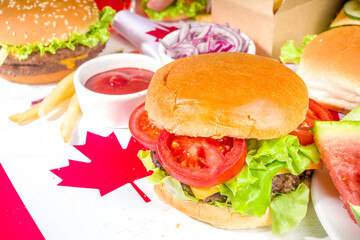 Set of various Canada Day bbq food. Picnic party table with maple leaf shaped watermelon, flags, burgers, hot dogs, fries and sauces, cold drinks, white table with red decor, top view copy space