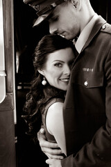Vintage couple, man in uniform, holds woman close to his chest as she looks at camera