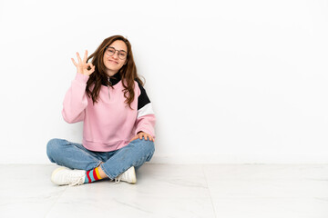 Young caucasian woman sitting on the floor isolated on white background showing ok sign with fingers