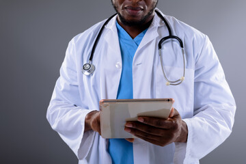 Mid section of african american male doctor using digital tablet against grey background - Powered by Adobe