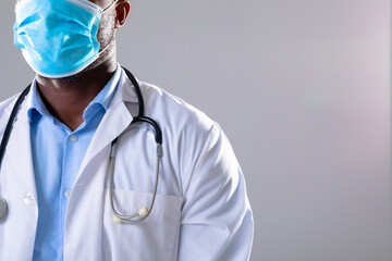 Mid section of african american male doctor wearing face mask against grey background - Powered by Adobe