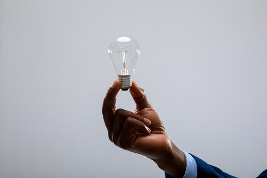 Close up of african american businessman holding light bulb against grey background