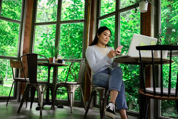 Young Asian woman in coffee shop using smartphone.