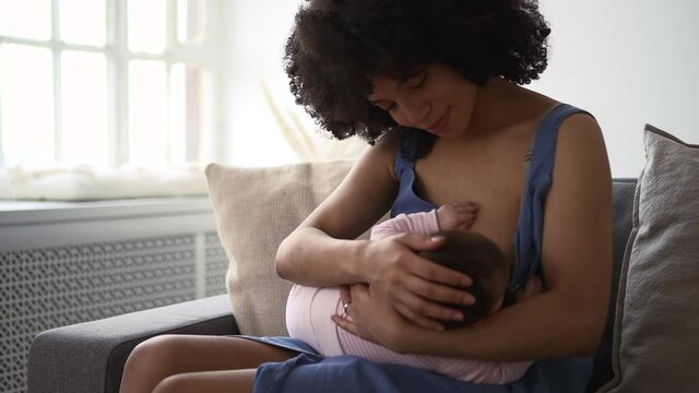 Mom breastfeeding little baby and enjoying motherhood, sitting on couch in home room spbd.